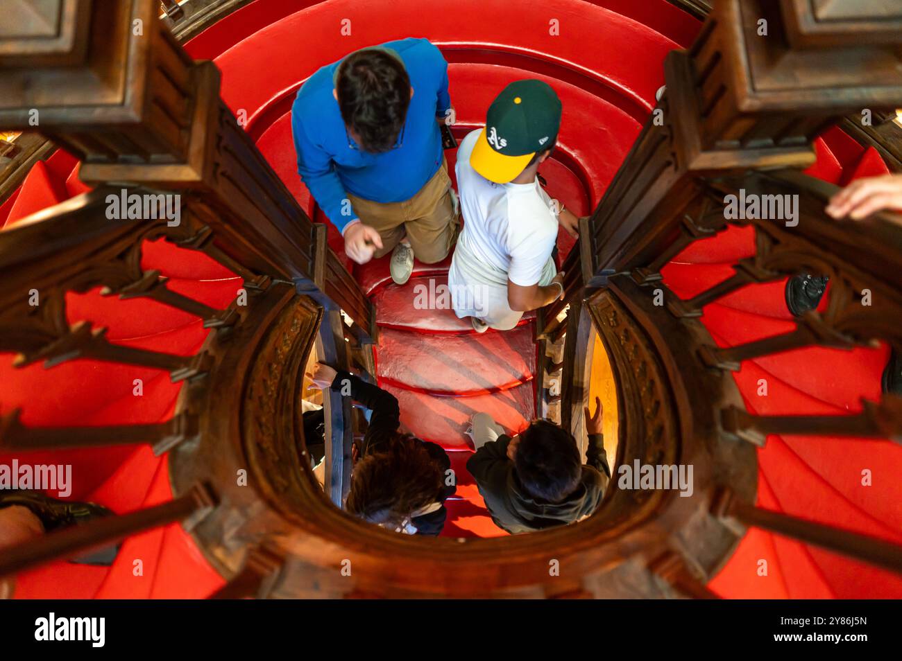 Porto, Portugal - 12. September 2024 : die Menschen bewegen sich über eine wunderschön gestaltete Wendeltreppe mit sattem rotem Teppich. Stockfoto