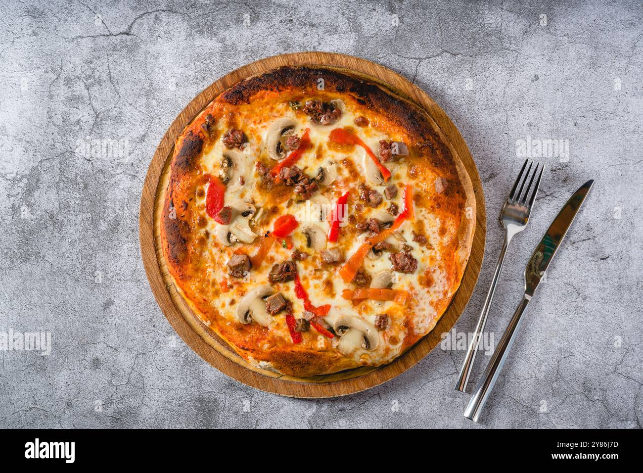 Pizza mit Paprika und Roastbeef auf dem Schneidebrett auf einem Steintisch Stockfoto