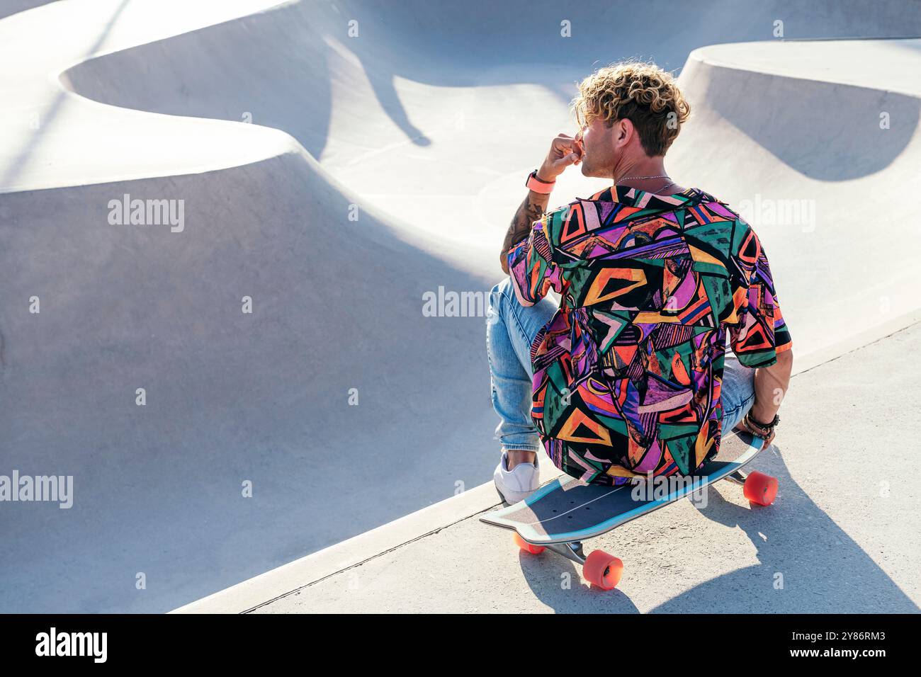 Ein Typ mit buntem Hemd sitzt auf Skateboard Stockfoto