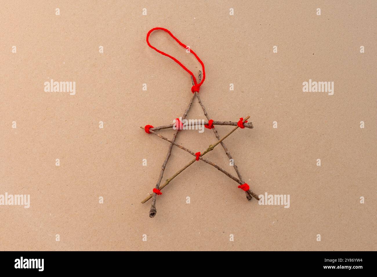 Ein fünfzackiger Stern aus Stäben, an den Punkten mit roter Schnur zusammengebunden. Der Stern hat einen rustikalen, handgefertigten Look, was ihn zu einer charmanten Ergänzung für Weihnachtsdekorationen oder Bastelprojekte macht. Stockfoto
