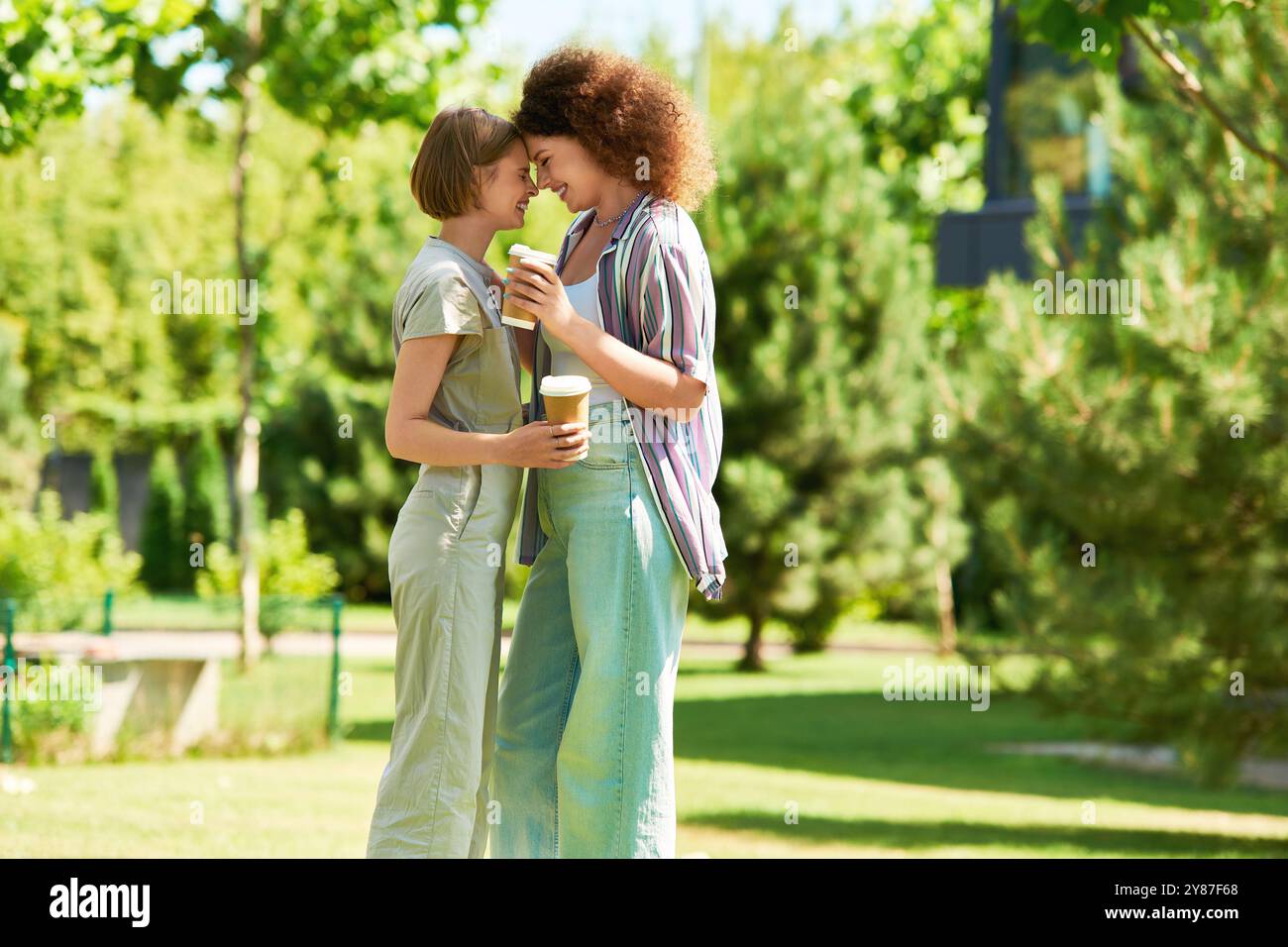 Zwei Freunde verbringen einen fröhlichen Moment in einem lebhaften Park, schlürfen Smoothies und lächeln einander an. Stockfoto