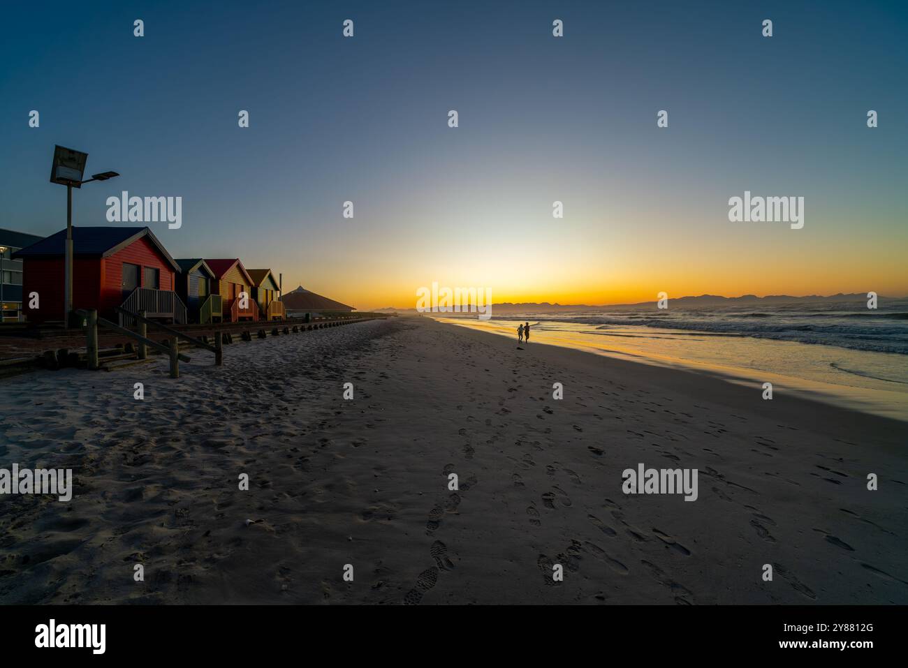 Kapstadt, Südafrika - 31. August 2022: Menschen laufen am Muizenberg Beach, neben den farbenfrohen Strandhütten, in Kapstadt, Südafrika Stockfoto