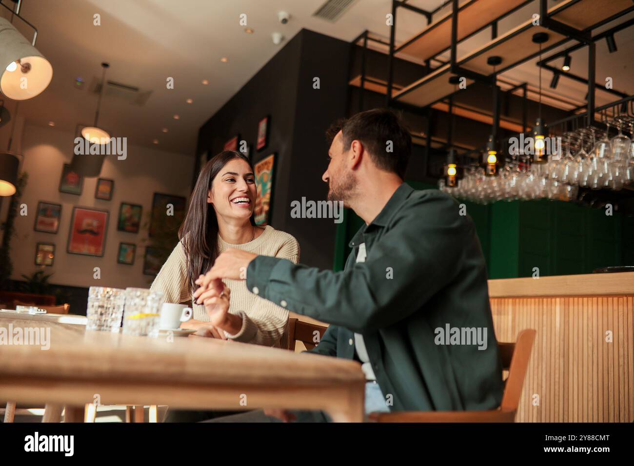 Zwei Freunde teilen sich Lachen und warme Drinks in einem charmanten Café und schaffen eine einladende Atmosphäre, die an einem sonnigen Tag die Verbindung und Freude feiert Stockfoto