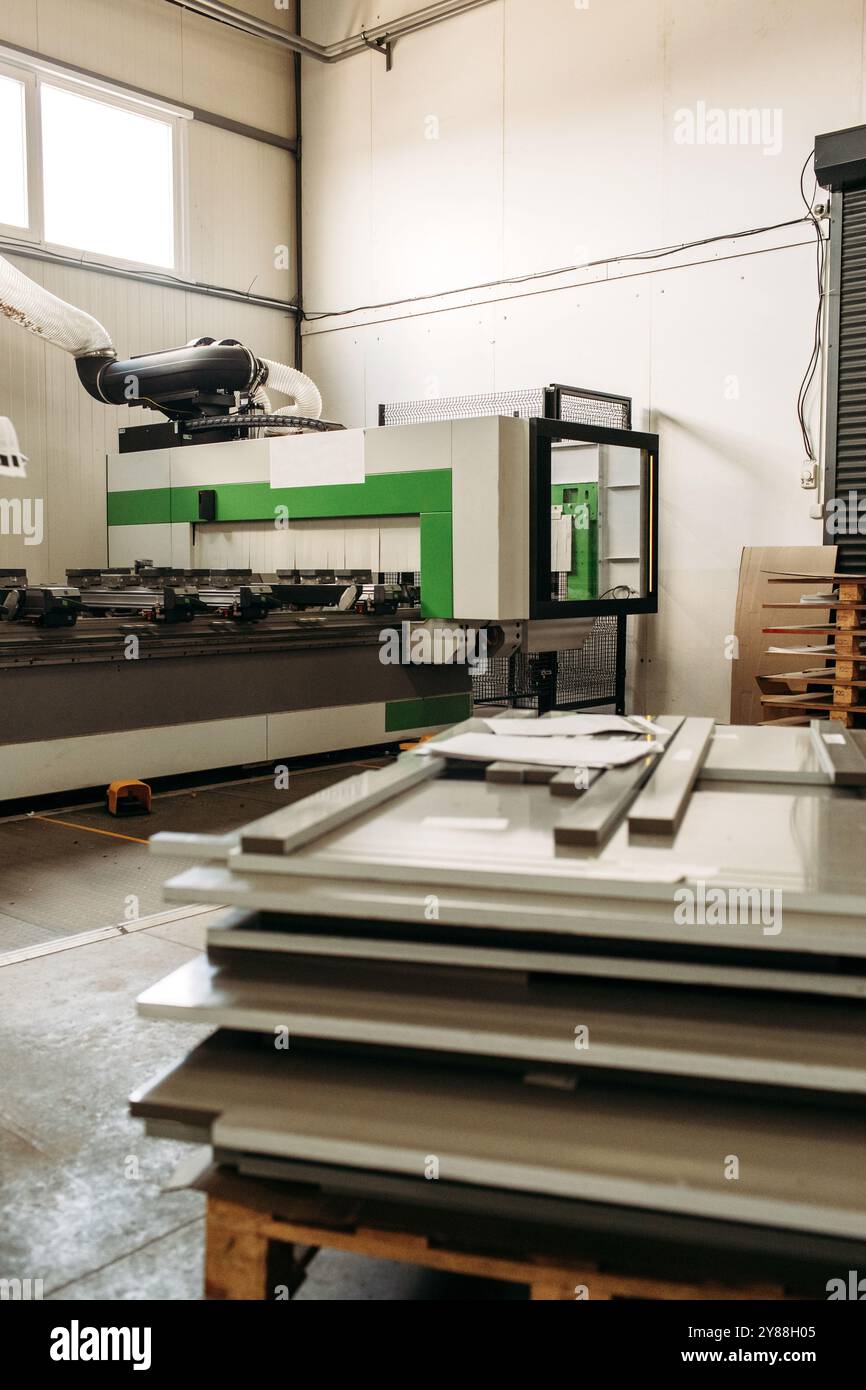 Frisch geschnittene Holzplatten stapeln sich neben einem CNC-Router in einer hellen Fabrik. Die Maschine wird zum präzisen Schneiden in der Möbelproduktion verwendet Stockfoto