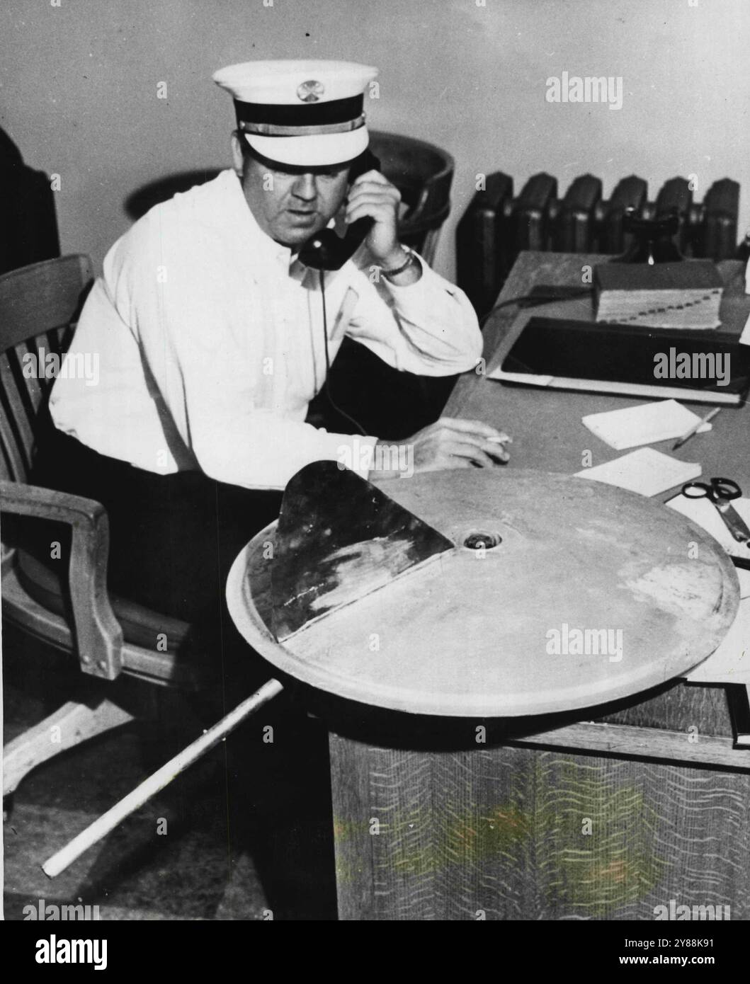 „Jemand hat sich für einen Witz eine Menge Mühe gemacht“, meinte Feuerwehrchef Wallage Newcomb über die 30-Zoll-galvanisierte Eisenscheibe (auf dem Schreibtisch), die im Juli 1947 in jemandes Garten in North Hollywood, Kalifornien, landete. Das Gerät hatte in der Mitte eine Radioröhre, ein Auspuffrohr und eine senkrechte Lamelle. August 1952. (Foto von United Press). Stockfoto