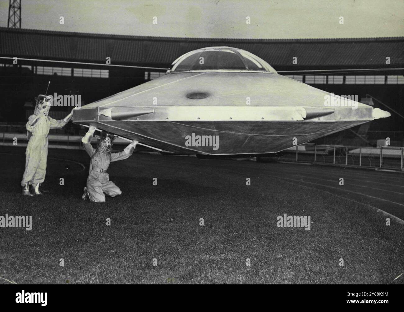 Besucher vom Mars: Die beiden Marsmenschen werden bei ihrem Tätowierungsakt in der Weißen Stadt gesehen, wie sie nach ihrer Ankunft in der Arena aus ihrer Flying Untertasse steigen. Da steht der 15-jährige Brian Sheppard, während seine 23-jährige W.R.A.F.-Angestellte Molly Day gerade aus der Untertasse kommt. Ein neuartiges Feature von This Year Searchlight Tattoo, das vom 4. Bis 8. Juli in der White City stattfindet. , Wird die Landung einer fliegenden Untertasse sein, von der aus zwei Besucher vor dem Mars kommen. Dieser „Aping Saucer“, der allen Traditionen der Science-Fiction treu ist, wurde vom R.A.F. Maintenance Command, UXB, gebaut Stockfoto