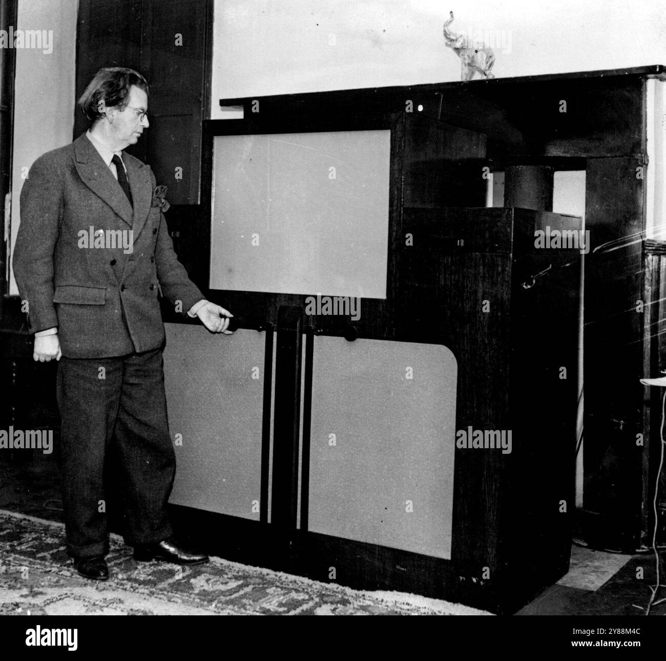 Fortschritte in der Kriegszeit im Fernsehen – John Logie Baird, der berühmte Pionier des Fernsehens, wird hier mit dem Ergebnis seiner Kriegsexperimente gesehen, das aktuellste Fernsehempfangsgerät, das erst nach dem Krieg auf dem Markt sein wird. Es ist ein ziemlich großes Möbelstück und hat einen großen Bildschirm im Vergleich zu den älteren Modellen. Sie erhält Farbe und die Bilder heben sich in Relief hervor. November 1946. (Foto von Keystone). Stockfoto