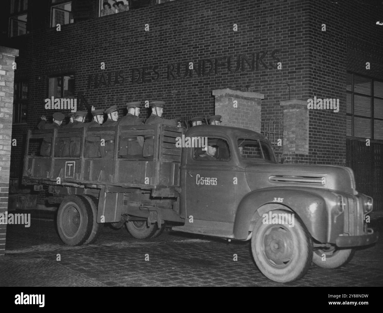 Old Guard verlässt Radio Berlin -- sowjetische Tommy-Schützen verabschieden sich von ostdeutschen Kommunisten, als sie Radio Berlin im britischen Sektor verlassen, 19 Stunden nachdem die Briten eine siebentägige bewaffnete Blockade auf der sowjetisch kontrollierten Radiostation aufgehoben hatten. Eine neue Truppenabteilung war verspätet im selben LKW angekommen, um die alte Wache zu entlasten. Sechzehn Soldaten und ein Offizier gingen aus dem hinteren Tor des Gebäudes, während weibliche Angestellte ihre Köpfe aus einem Fenster im zweiten Stock heulten und jubelten. Juni 1952. (Foto von zugehörigem Pressefoto). Stockfoto