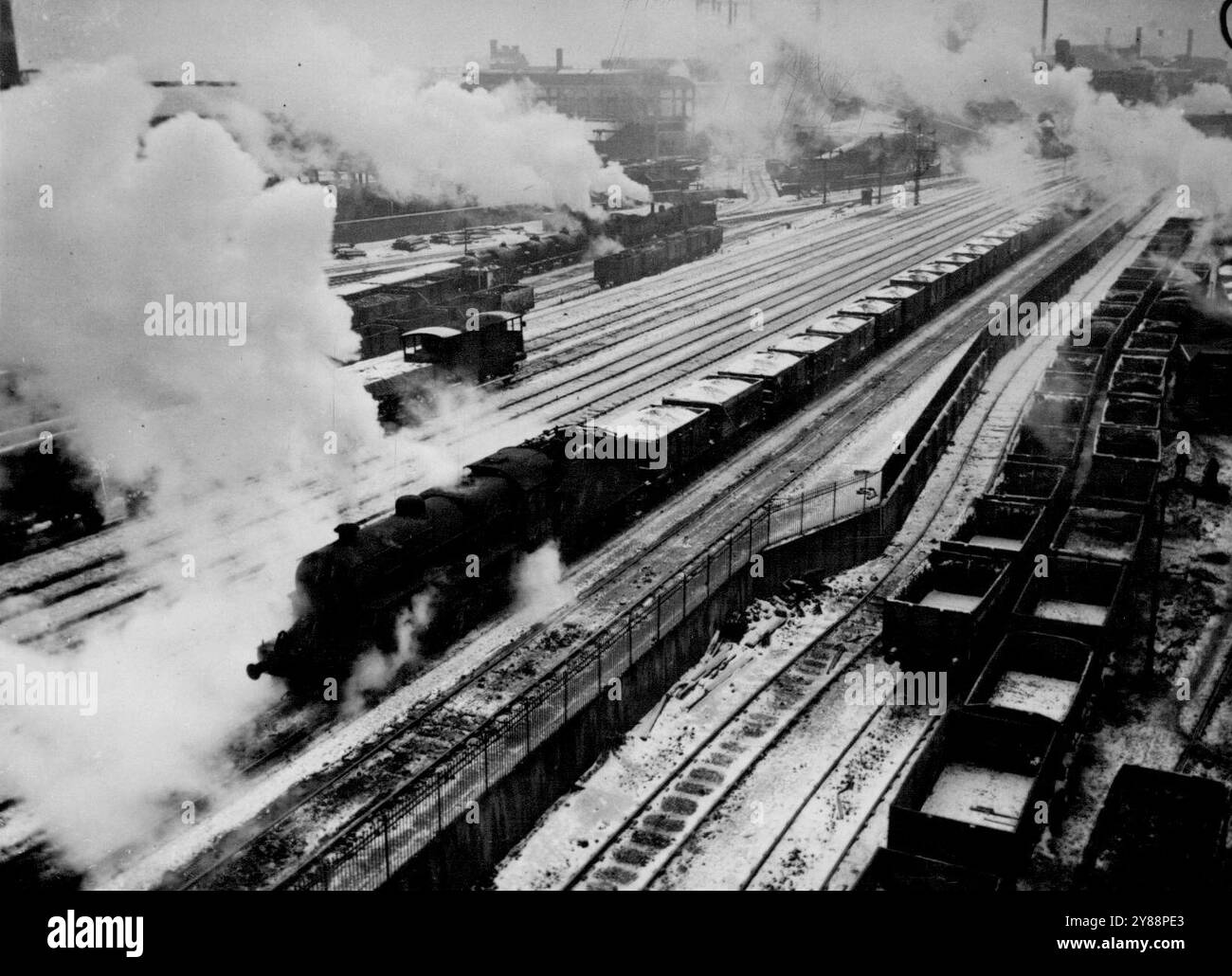 Mit Londons dringend benötigtem Treibstoff nach Süden rasen – Ein Zug, mit Kohle beladene Wagen, die mit Schnee bedeckt sind, rasen südlich von Birmingham, Warwickshire, England, 13. Februar. Rechts neben Foto der anderen Trucks, warten Sie auf den Rangierbahnhof. In ganz Großbritannien gab es Hunderte von Kohlewagen, die zuvor in Nordengland und den Midlands, Race South, eisgebunden waren. Innerhalb von 24 Stunden nach ihrem Ziel wurden sie entladen und sind auf dem Rückweg, um weiteren Treibstoff von den Collieries zu erhalten. Februar 1947. (Foto von zugehörigem Pressefoto). Stockfoto