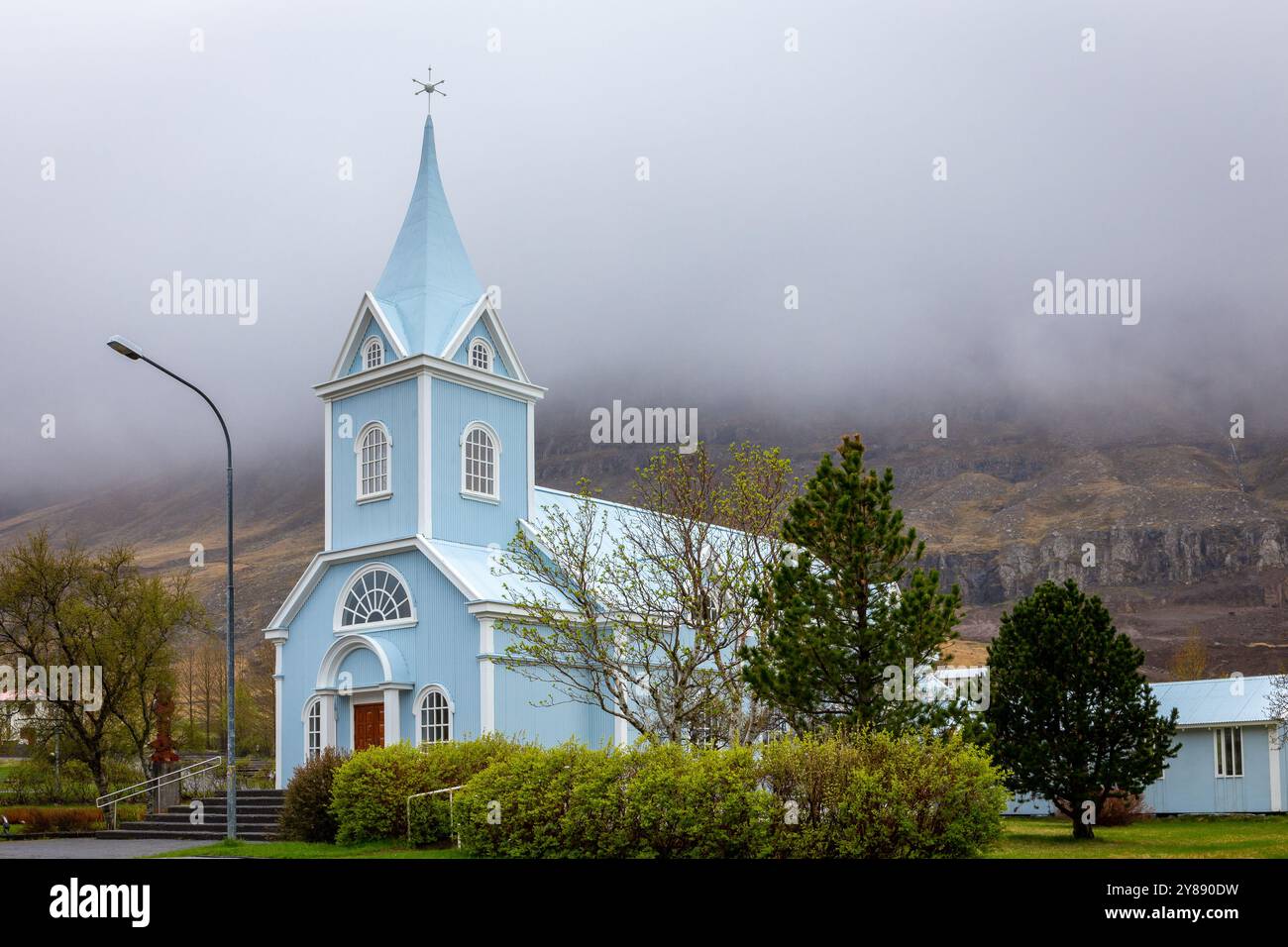 Die Blaue Kirche in Seydisfjordur (Seydisfjardarkirkja), Außenansicht der hellblauen Gebäudefassade mit grüner Vegetation rund um Island. Stockfoto