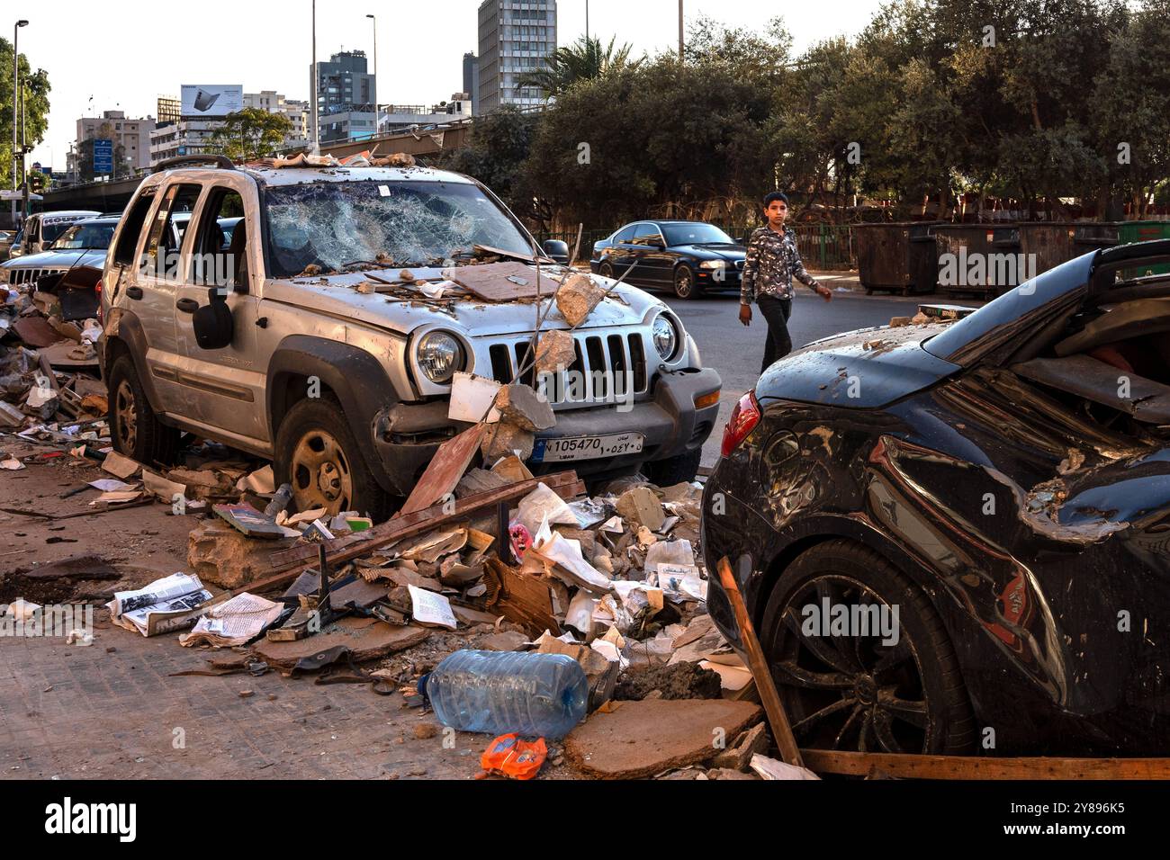Cola, Libanon. Oktober 2024. Ein Junge mit Militärjacke läuft an zwei Autos vorbei, die durch israelische Bombenangriffe beschädigt wurden, im Viertel Cola am Stadtrand von Beirut. Seit Beginn des Krieges zwischen der Hisbollah und Israel hat die ständige Bombardierung im Libanon bereits mehr als 1 Million Menschen vertrieben und 1.400 Menschen getötet. Quelle: SOPA Images Limited/Alamy Live News Stockfoto
