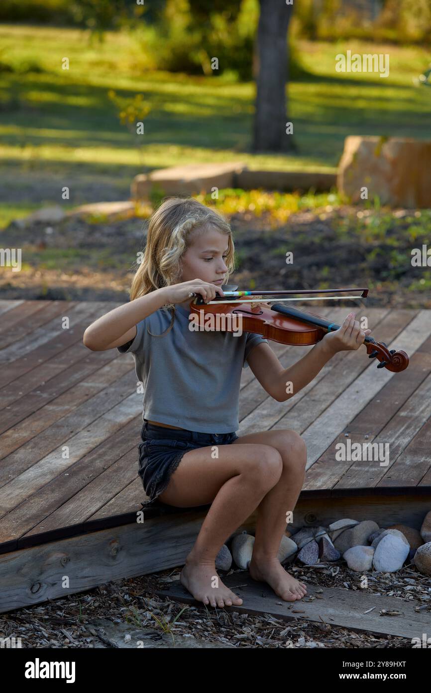Das Mädchen spielt Geige, während es auf einem Deck sitzt Stockfoto