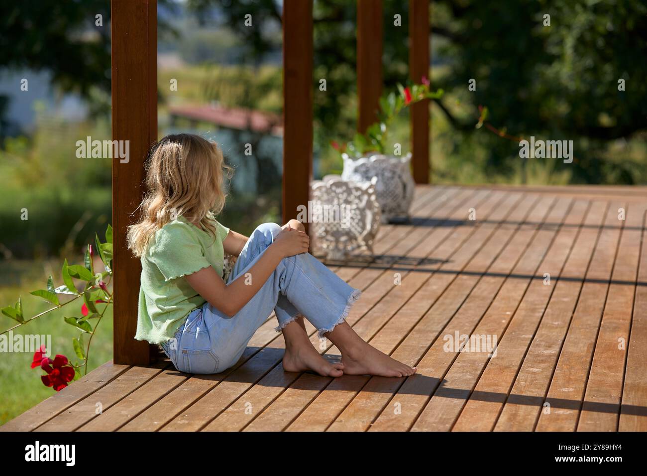 Ein Mädchen schaut weg, während es auf einem Holzdeck sitzt Stockfoto