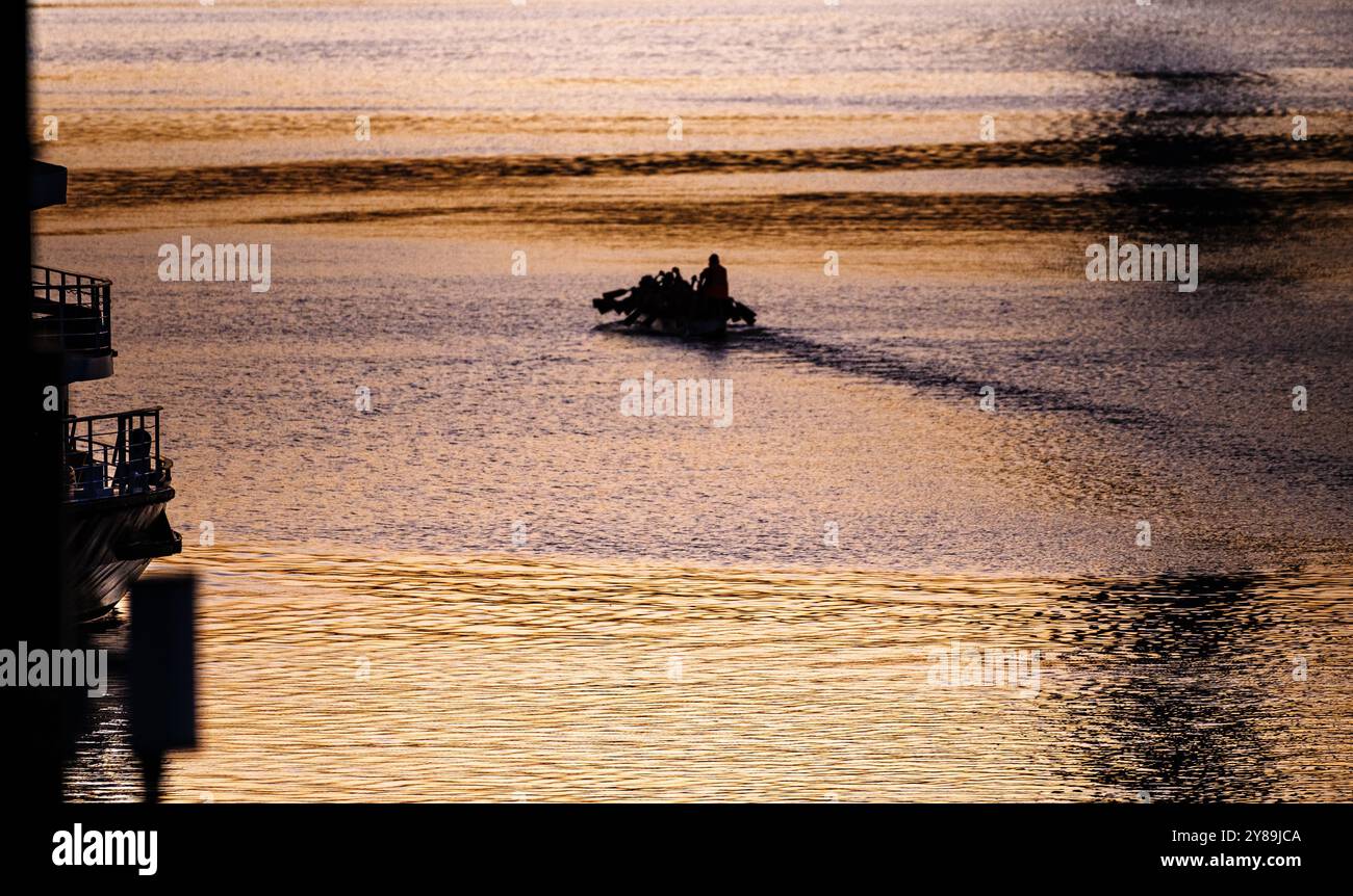 Silhuette von Menschen, die das Boot im Victoria Harbour in der Abenddämmerung rudern, mit hübscher Farbe des Sonnenuntergangs, die auf der Wasseroberfläche in Melbourne, Victoria, Australien, abfällt Stockfoto