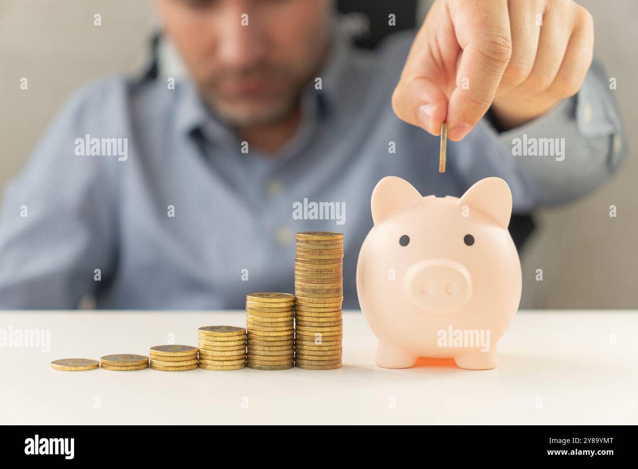 Geschäftsmann, der eine Münze in einer Sparkasse hält. Das Aufstellen von Münzen in einer Reihe von niedrig nach hoch ist vergleichbar mit dem Einsparen von Geld, um mehr zu wachsen. Das Konzept des Wachstums Stockfoto
