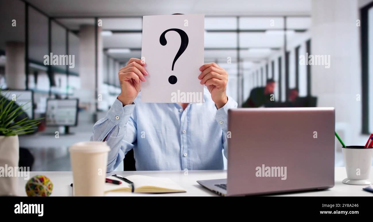 Geschäftsmann Mit Fragezeichen Vor Dem Gesicht Am Schreibtisch Im Büro Stockfoto