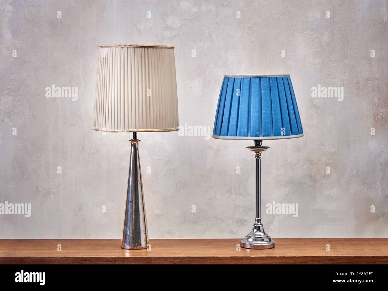 Retro-Lampen mit Metallkörpern in Beige- und Blautönen, die auf Holztisch vor schäbigen Wänden platziert werden Stockfoto