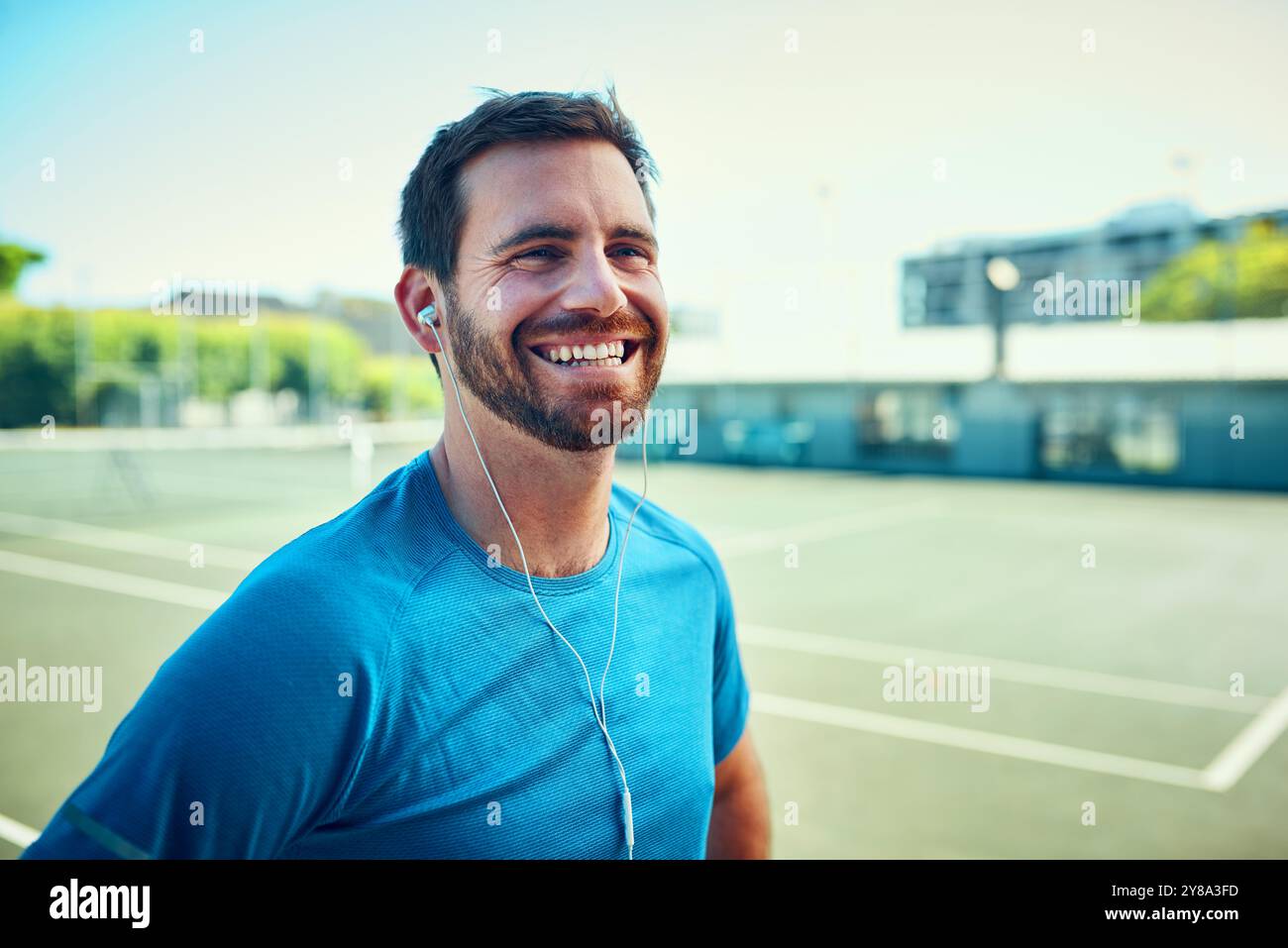 Tennisplatz, Sport und Mann auf Lächeln mit Ohrhörern während des Trainings oder Trainingspause. Männliche Person, draußen und entspannen Sie mit Freude mit Streaming Stockfoto