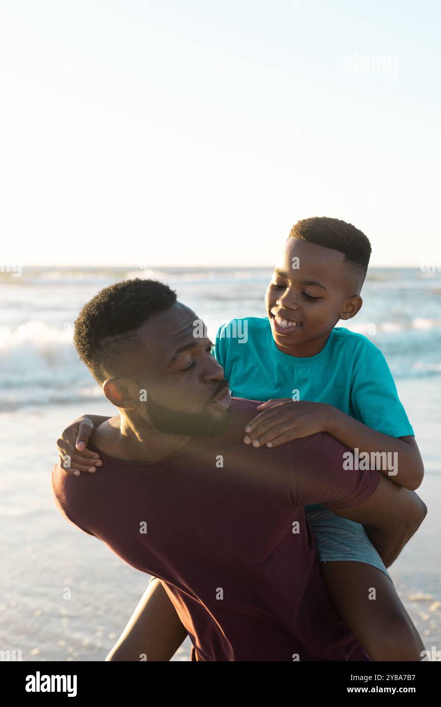 afroamerikaner Huckepack verspielter Sohn gegen wunderschönes Meer und Himmel während Sonnenuntergang Stockfoto