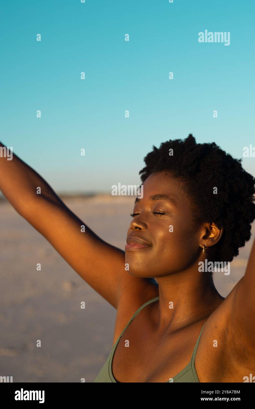 Nahaufnahme einer afroamerikanischen mittelerwachsenen Frau mit geschlossenen Augen, die Arme hochhebt und am Strand genießt Stockfoto