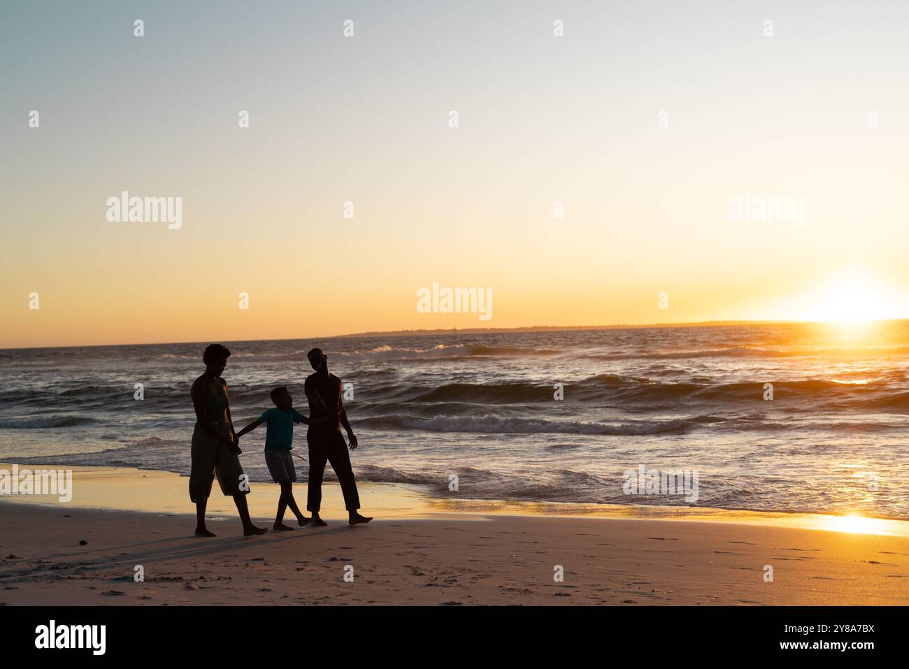 Silhouette afroamerikanischer Junge mit Mutter und Vater, der bei Sonnenuntergang am Strand gegen den Himmel spaziert Stockfoto