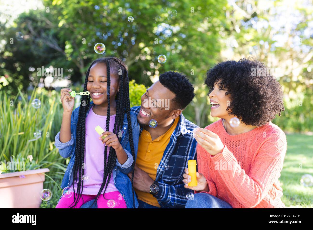 Glücklicher afroamerikanischer Vater, Mutter und Tochter blasen Blasen in sonnigem Garten, Kopierraum Stockfoto