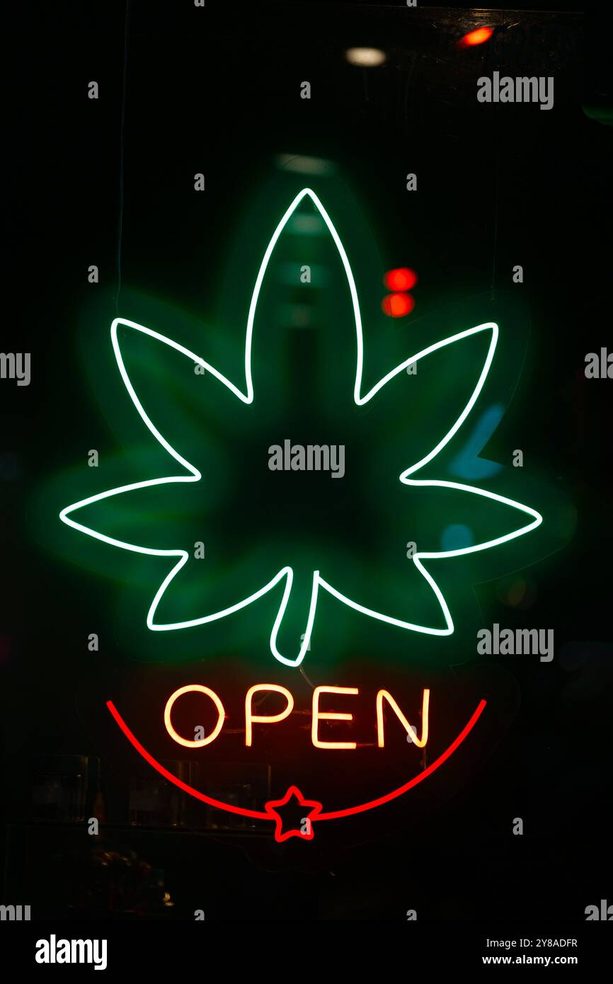 Ein Neonschild in einem Ladenfenster in Form eines Cannabisblattes mit dem Wort „Open“ darunter. Stockfoto