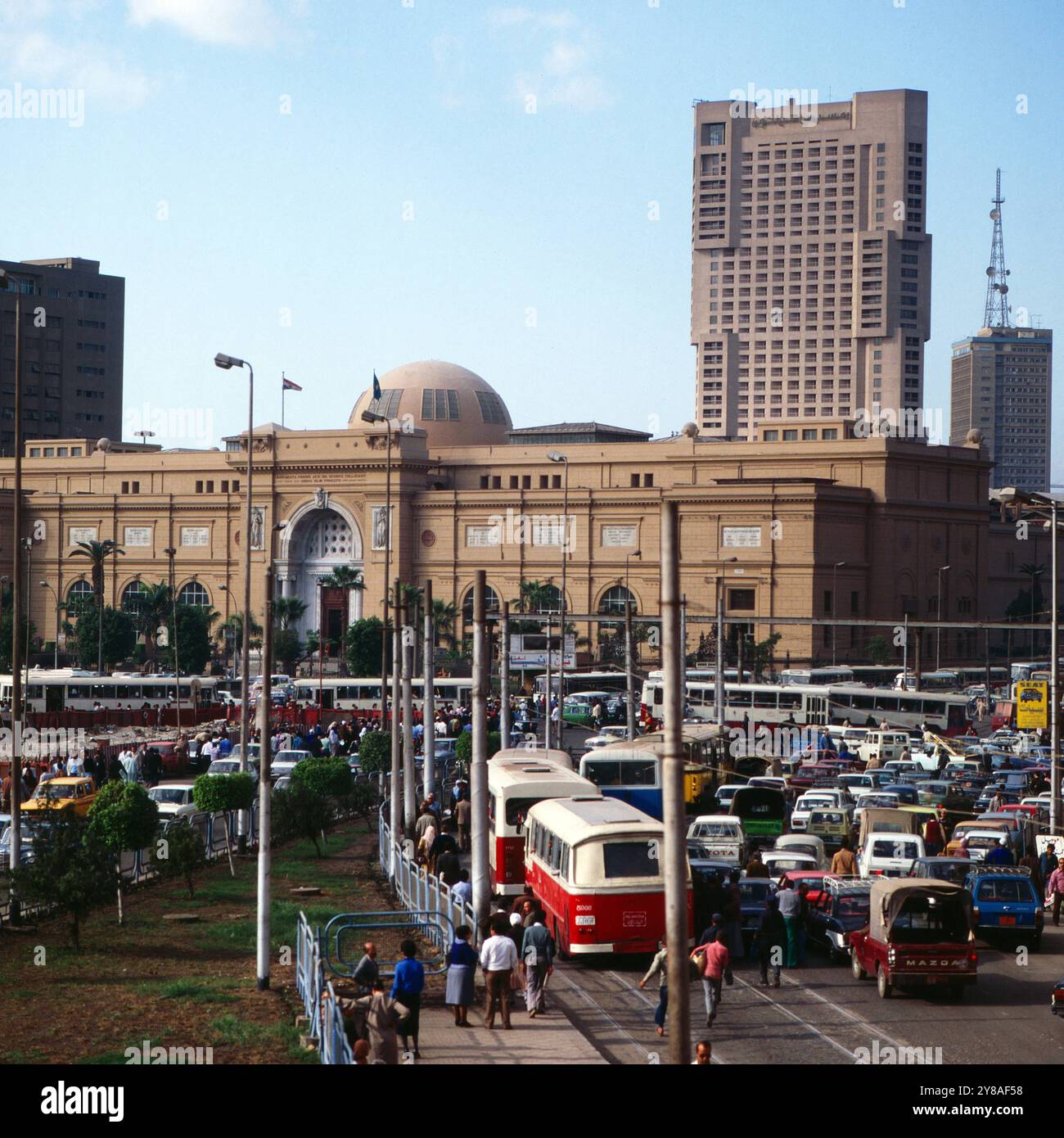 Tägliches Verkehrschaos auf der Meret Basha Straße mit Blick auf das Ägyptische Museum Kuppel und den Ramses Hotelturm in Kairo, nahe vom Midan al Tahrir Platz, Ägypten um 1987. 90010000176 Stockfoto