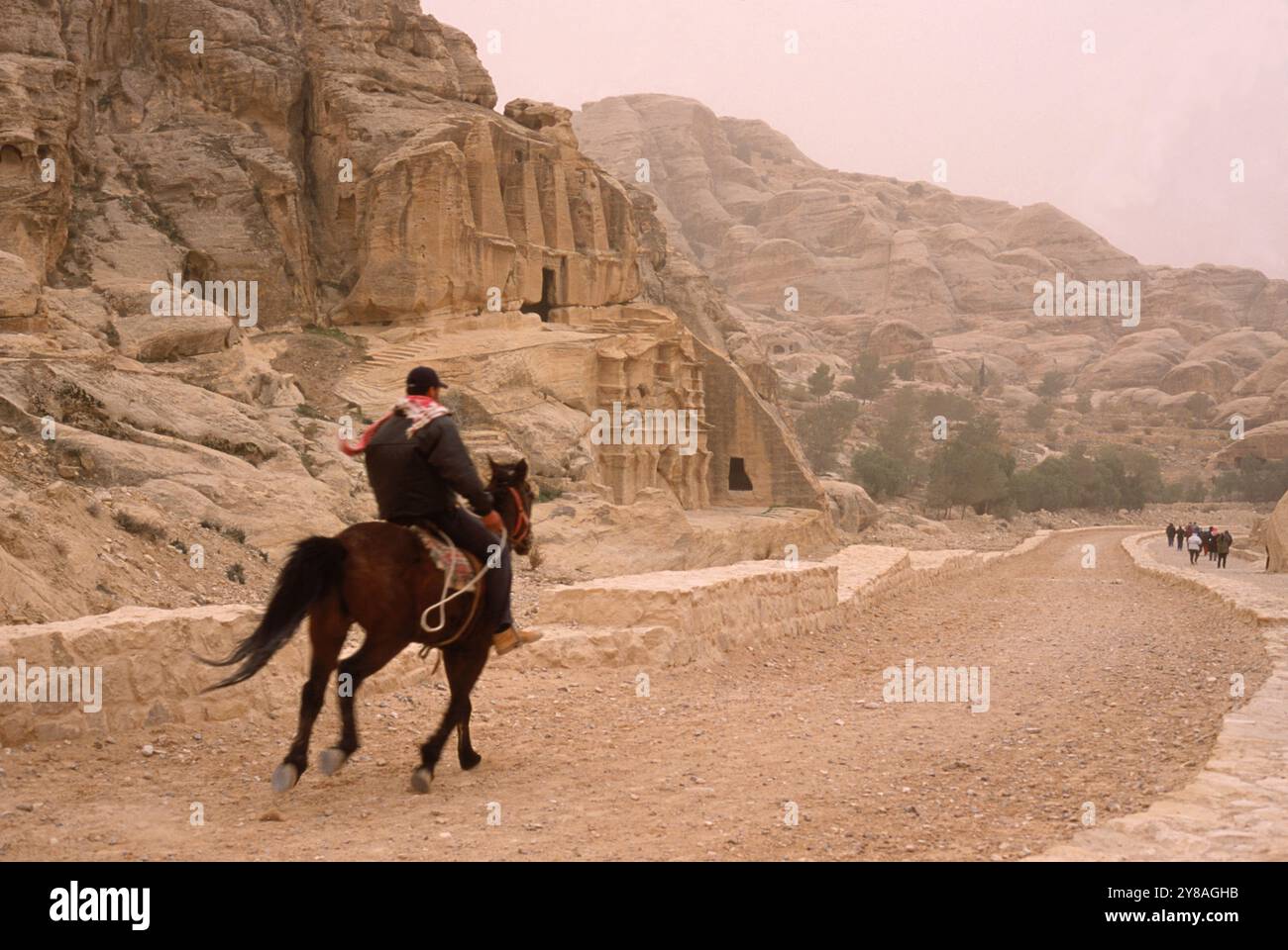 Ein Beduinenführer galoppiert zu Pferd in die historische römische Stadt Petra, Jordanien. Stockfoto