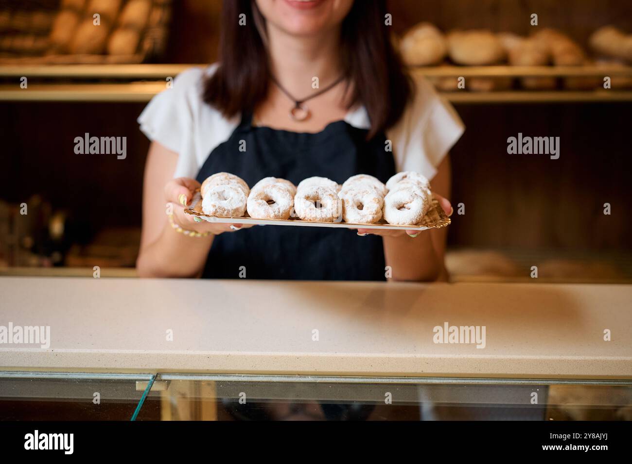 Eine lächelnde Frau präsentiert ein Tablett mit frisch gebackenem Gebäck in einer Bäckerei Stockfoto