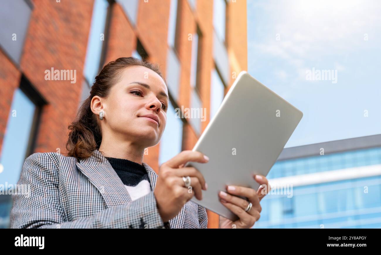 Professionelle Frau, die im Freien steht, ein digitales Tablet benutzt, mit einem modernen Gebäude im Hintergrund Stockfoto