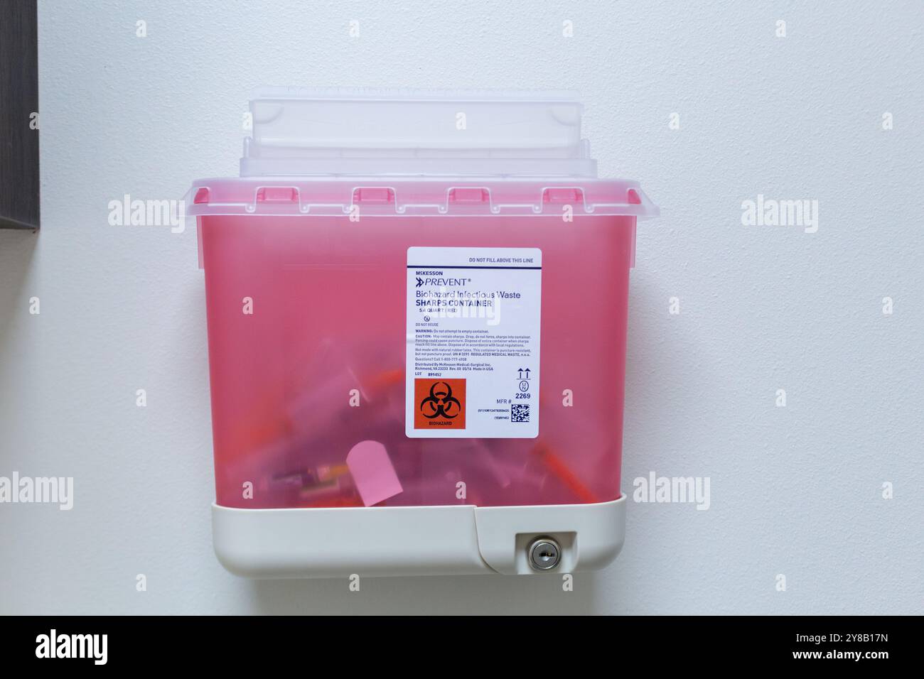 Verschlossener klarer rosafarbener Behälter für infektiösen Abfall für biologische Gefahrstoffe an der Wand einer medizinischen Praxis. Stockfoto