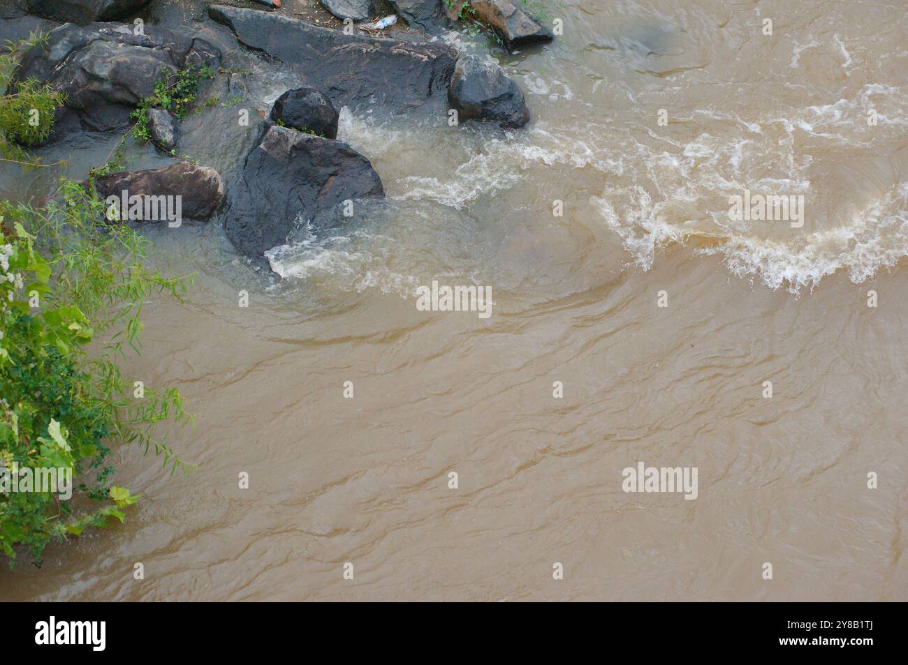 Close Up Overhead Blick hinunter auf die Flussfelsen in einem schnell bewegenden, schlammigen, braunen Fluss, der mit weißen Kappen rollte. Aggresse Stockfoto