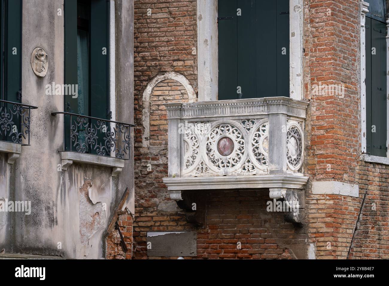 Fassade mit Fenstern und Balkon aus geschnitztem Stein in Venedig. Gemeißelter Steinbalkon eines alten venezianischen Gebäudes. Stockfoto