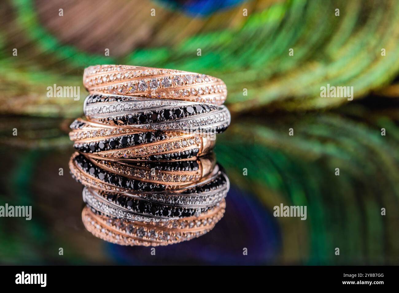 Eheringe werden im Spiegel reflektiert. Ein Satz von drei Ringen auf einem Hintergrund aus Pfauenfedern. Gold- und Silberringe mit schwarzen und weißen Steinen Stockfoto