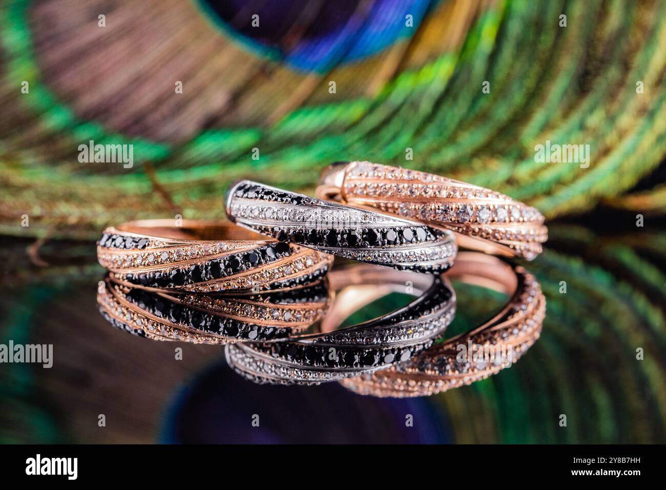 Eheringe werden im Spiegel reflektiert. Ein Satz von drei Ringen auf einem Hintergrund aus Pfauenfedern. Gold- und Silberringe mit schwarzen und weißen Steinen Stockfoto