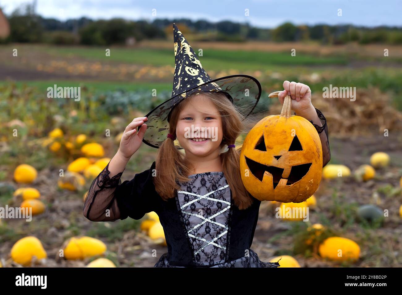 Kleines Mädchen in Hexenkostüm spielt im Herbstpark. Kind hat Spaß an Halloween Trick or Treat. Kinder tricksen oder behandeln. Kleinkind mit Jack-o-lan Stockfoto