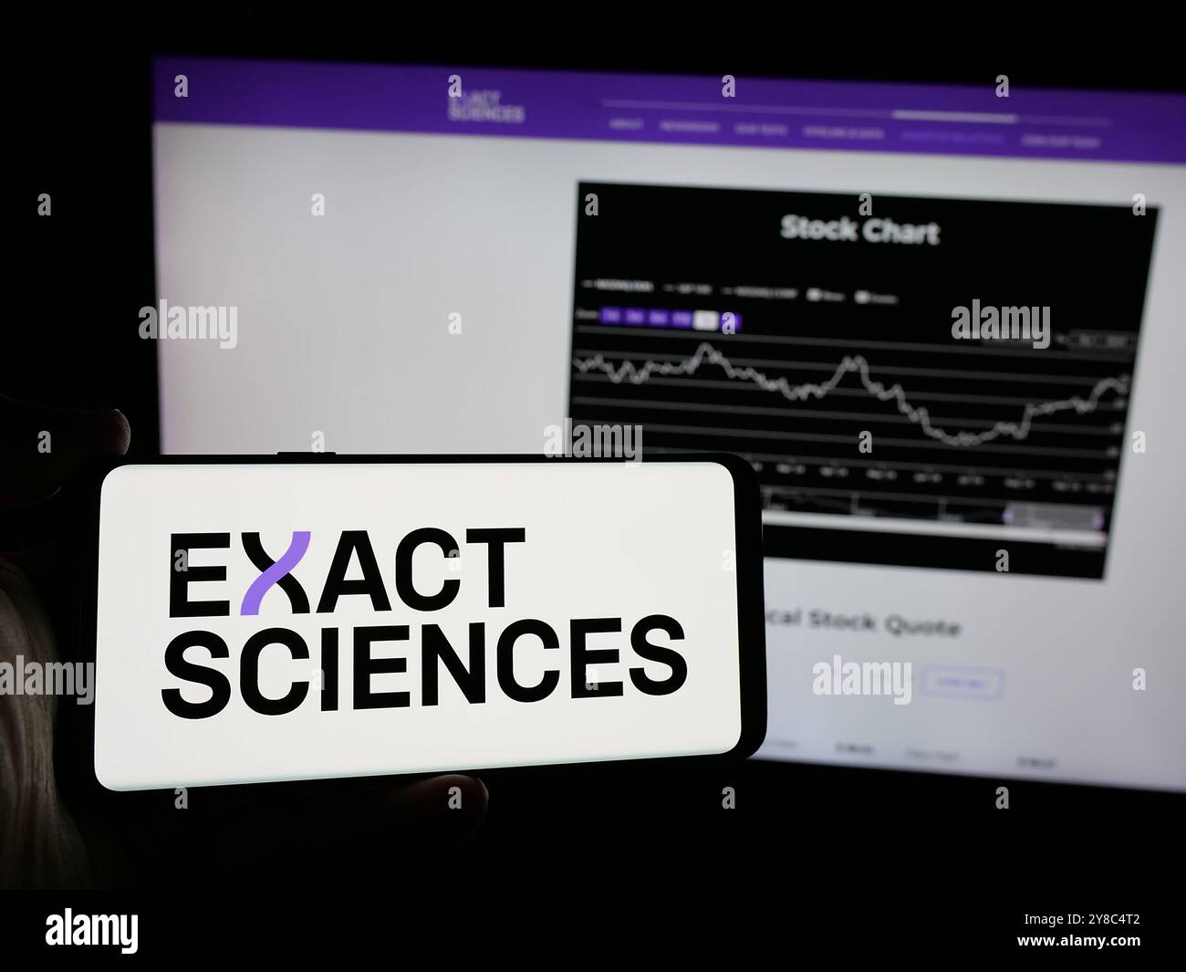 Person, die ein Mobiltelefon mit dem Logo des US-Biotech-Unternehmens Exact Sciences Corporation auf dem Bildschirm vor der Webseite hält. Schwerpunkt auf dem Display des Telefons. Stockfoto