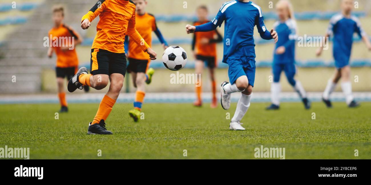 Kinder als Fußballspieler, die mit Ball laufen. Fußballer, Die Das Play League-Spiel Während Des Sunny Day Spielen. Zwei Teams im Sportwettbewerb. Teenager Soc Stockfoto