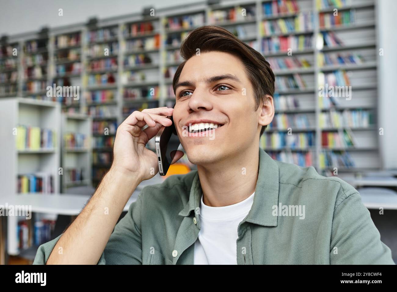 Ein fokussierter Schüler lächelt am Telefon und taucht in seine Studien in einer lebendigen Bibliothek ein. Stockfoto