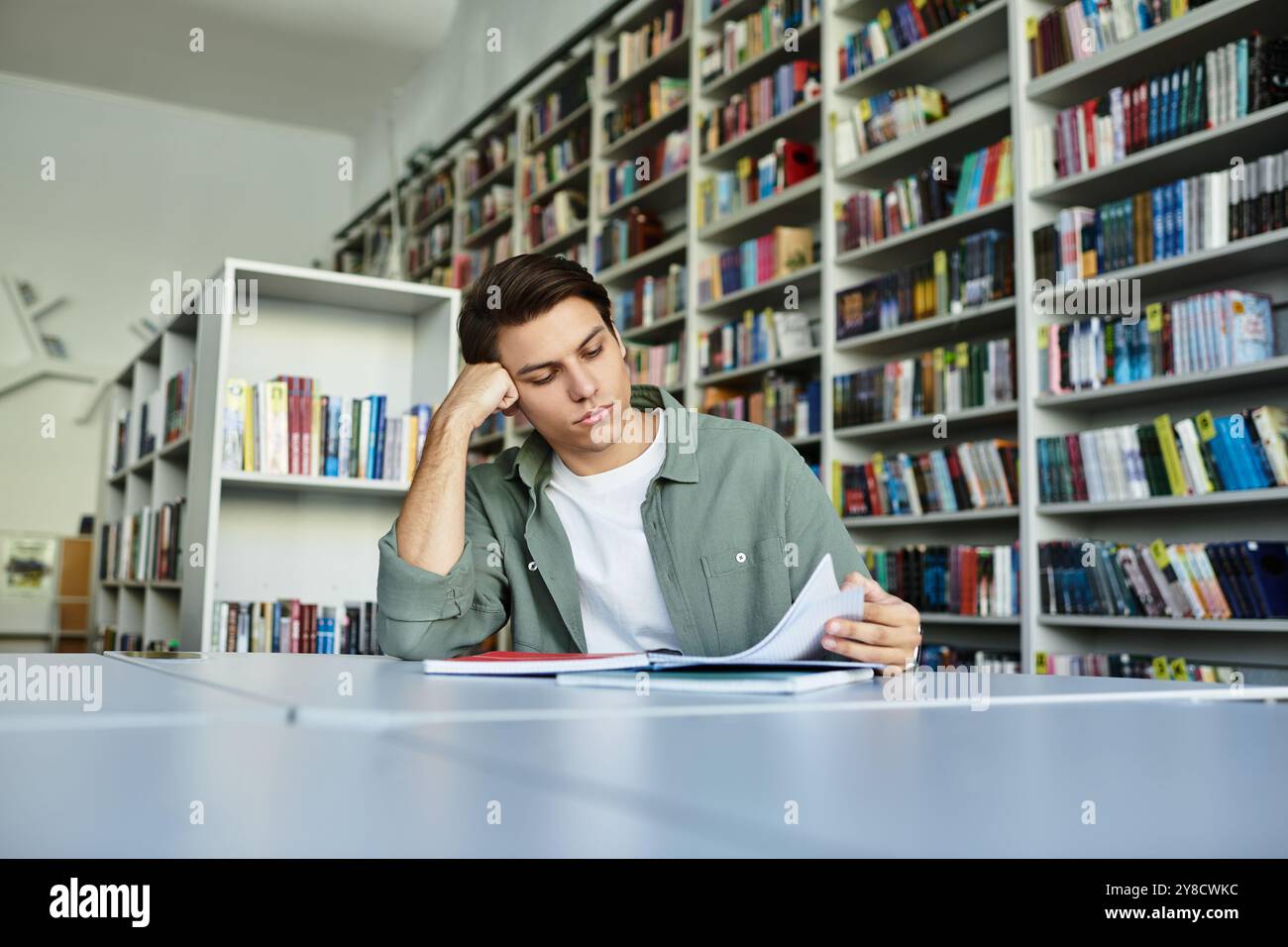 Ein fokussierter Student, der sich in einer lebhaften Bibliotheksatmosphäre intensiv mit seinem Studium beschäftigt. Stockfoto