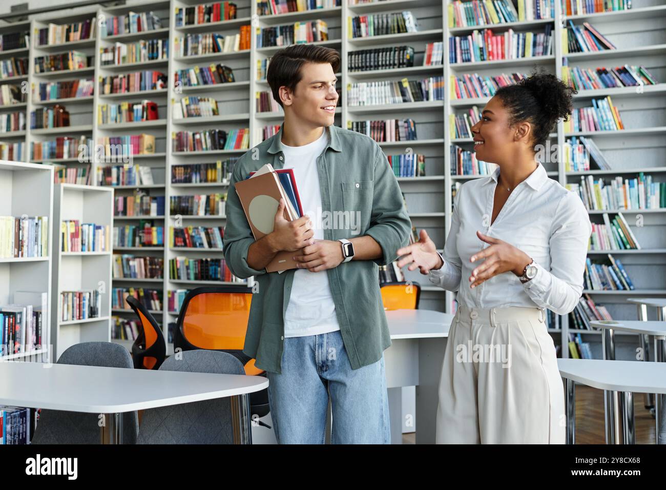 Eine engagierte Lehrerin teilt ihr Wissen mit ihrer aufmerksamen Schülerin in einer lebhaften Bibliotheksatmosphäre. Stockfoto