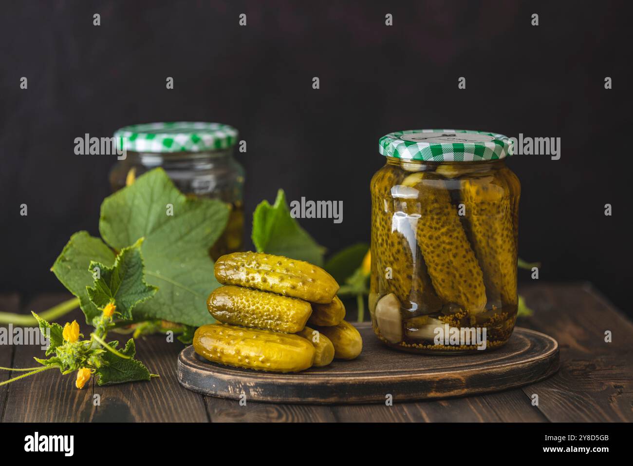 Glasgläser gefüllt mit knusprigen Gurken, ruhen auf einem rustikalen Holztisch mit frischen Zutaten und schaffen eine optisch ansprechende Szene Stockfoto