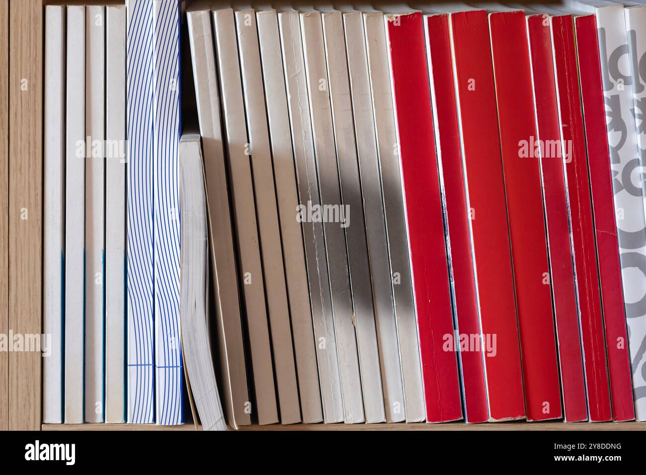 Organisierte Sammlung von Büchern auf einem hölzernen Bücherregal. Bücher, die ordentlich in einem Regal angeordnet sind, mit einer Vielzahl von Farben und Texturen, ideal für Präsentationen Stockfoto