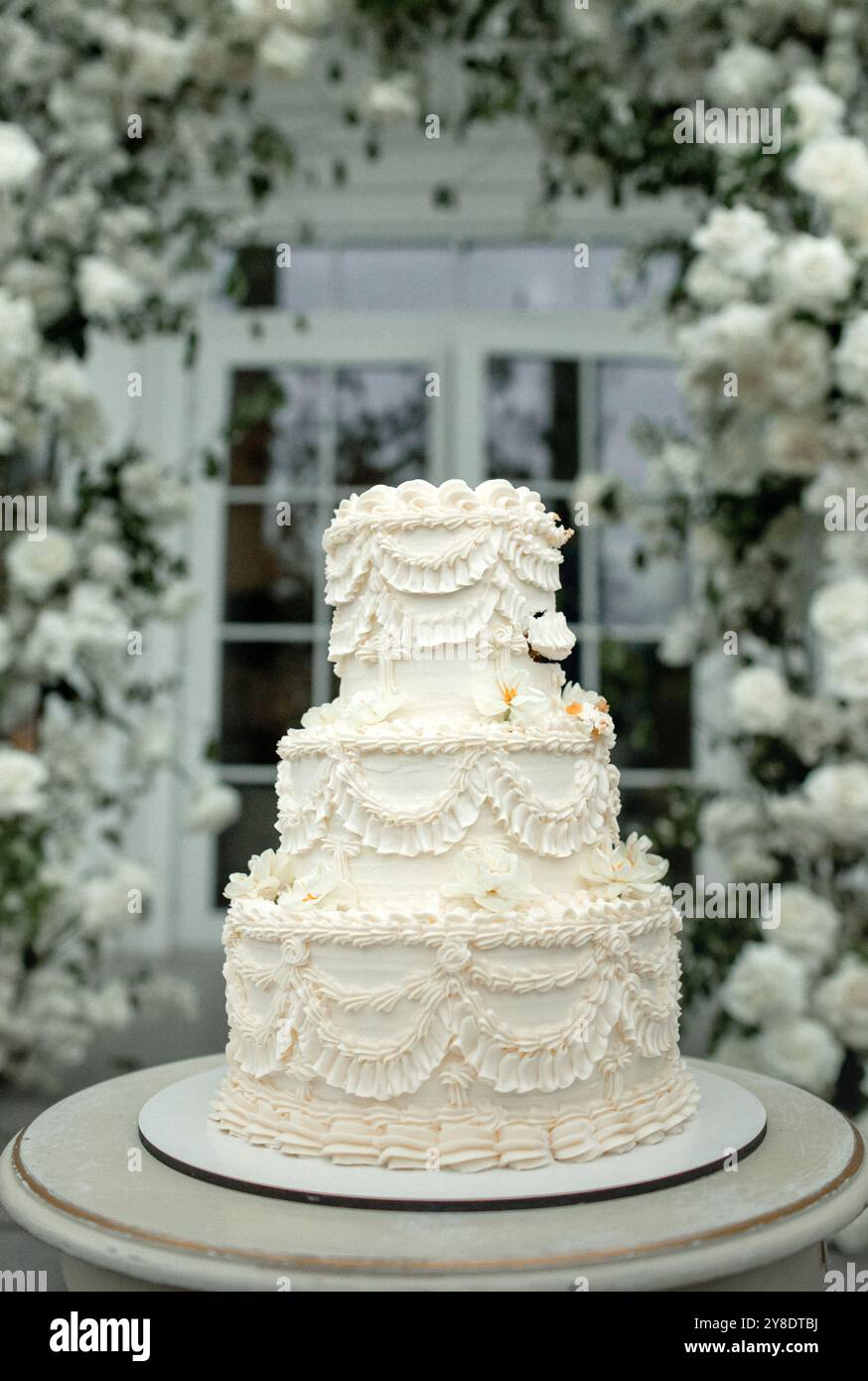 Eine wunderschön gefertigte Hochzeitstorte steht hoch und zeigt zarte Zuckerguss-Details, während eine Schicht geschnitten ist, sodass feuchte Schichten mit reichhaltigem Flav sichtbar werden Stockfoto