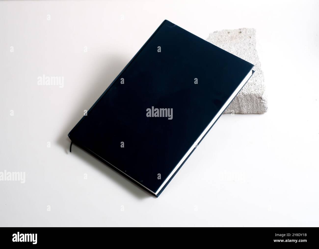 Ein stilvolles schwarzes Buch, das elegant auf einem sauberen weißen Steinhintergrund positioniert ist. Dieses minimalistische Design betont die schlanke Hülle und die vielseitige Natu Stockfoto