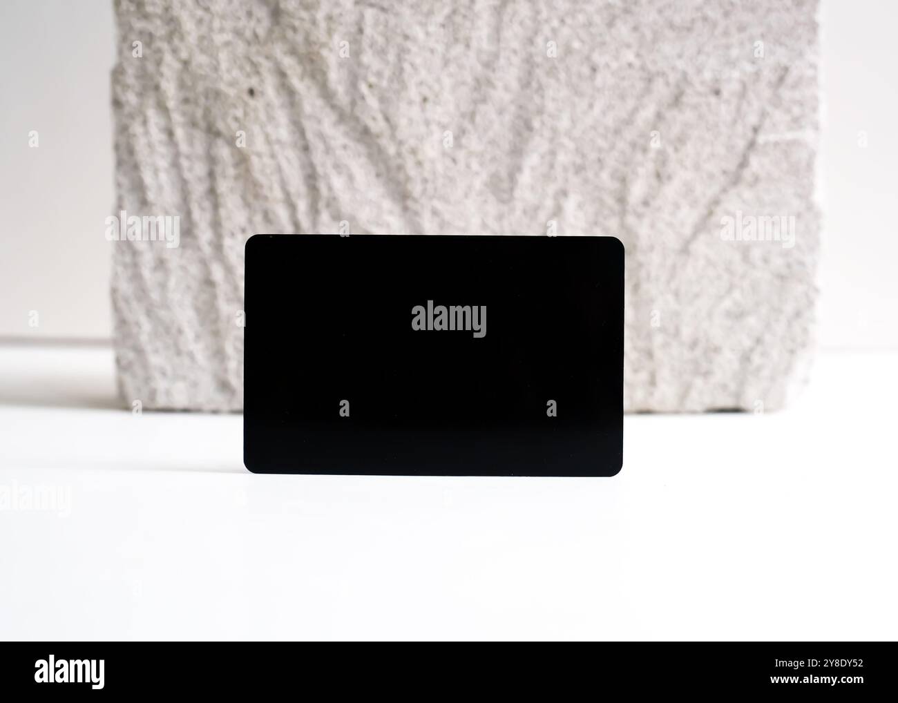 Ein raffiniertes Modell mit schwarzer Karte, das elegant vor einem sauberen weißen Steinhintergrund dargestellt wird. Dieses minimalistische Design unterstreicht das schlanke Design Stockfoto
