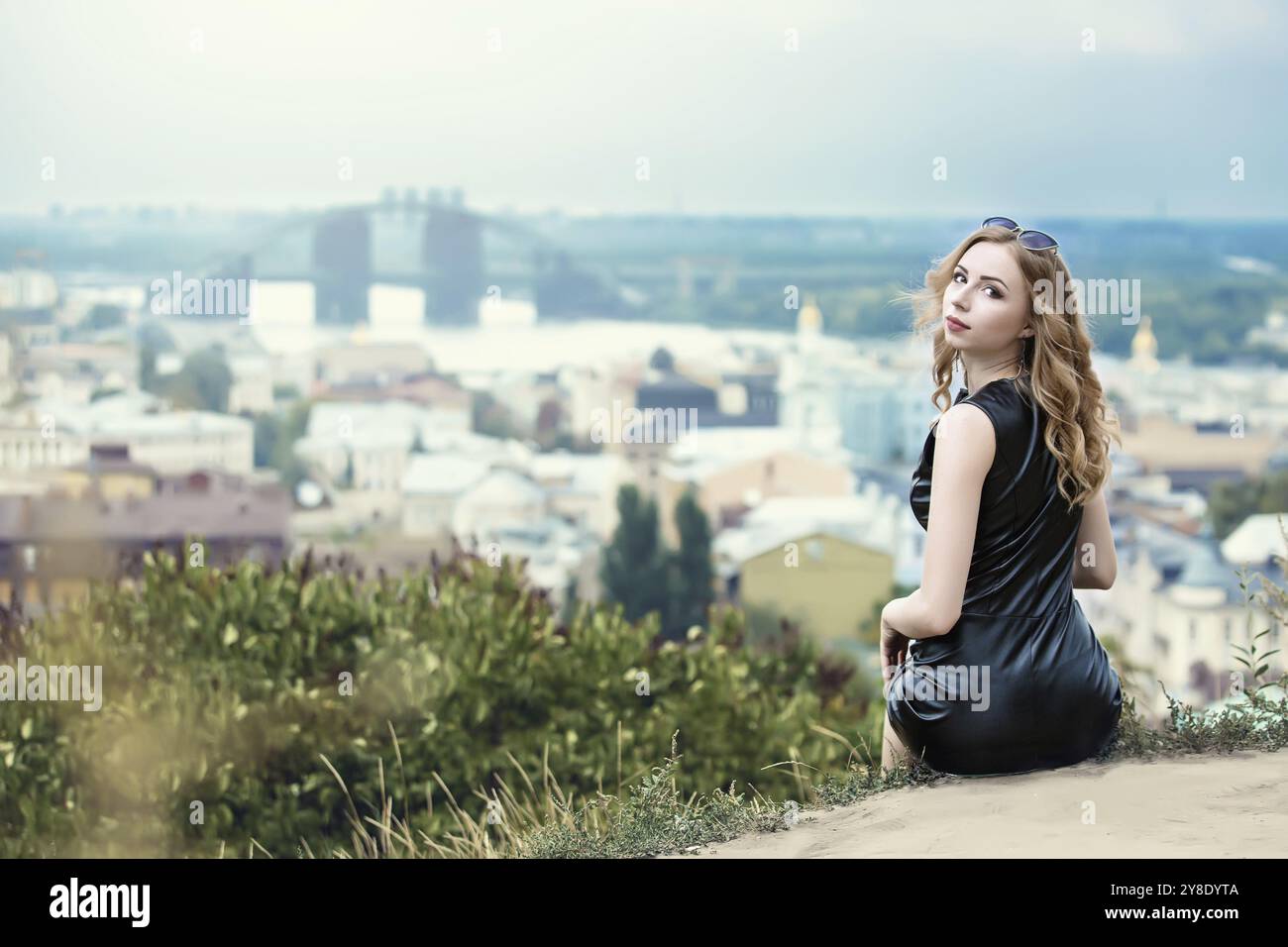 Die schöne einsame Mädchen im schwarzen Kleid und sunglassess sitzen auf dem Boden und ein Blick zurück Stockfoto