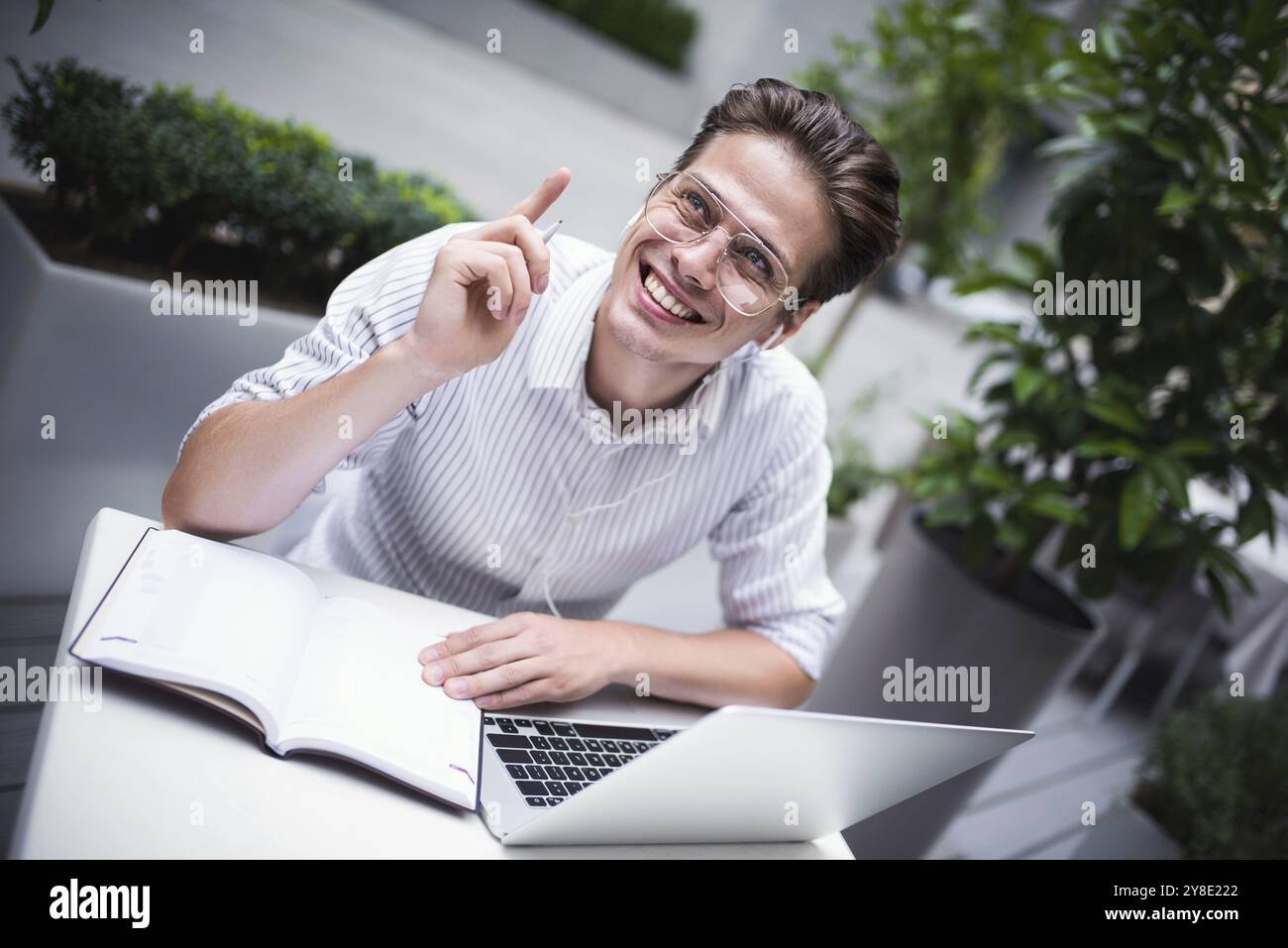 Ein glücklicher, gutaussehender Geschäftsmann mischt seine Pause und seinen Job im Freien, ein Geschäftsmann mit Kopfhörern schreibt neue Ideen in einem Notebook, das im Café sitzt Stockfoto