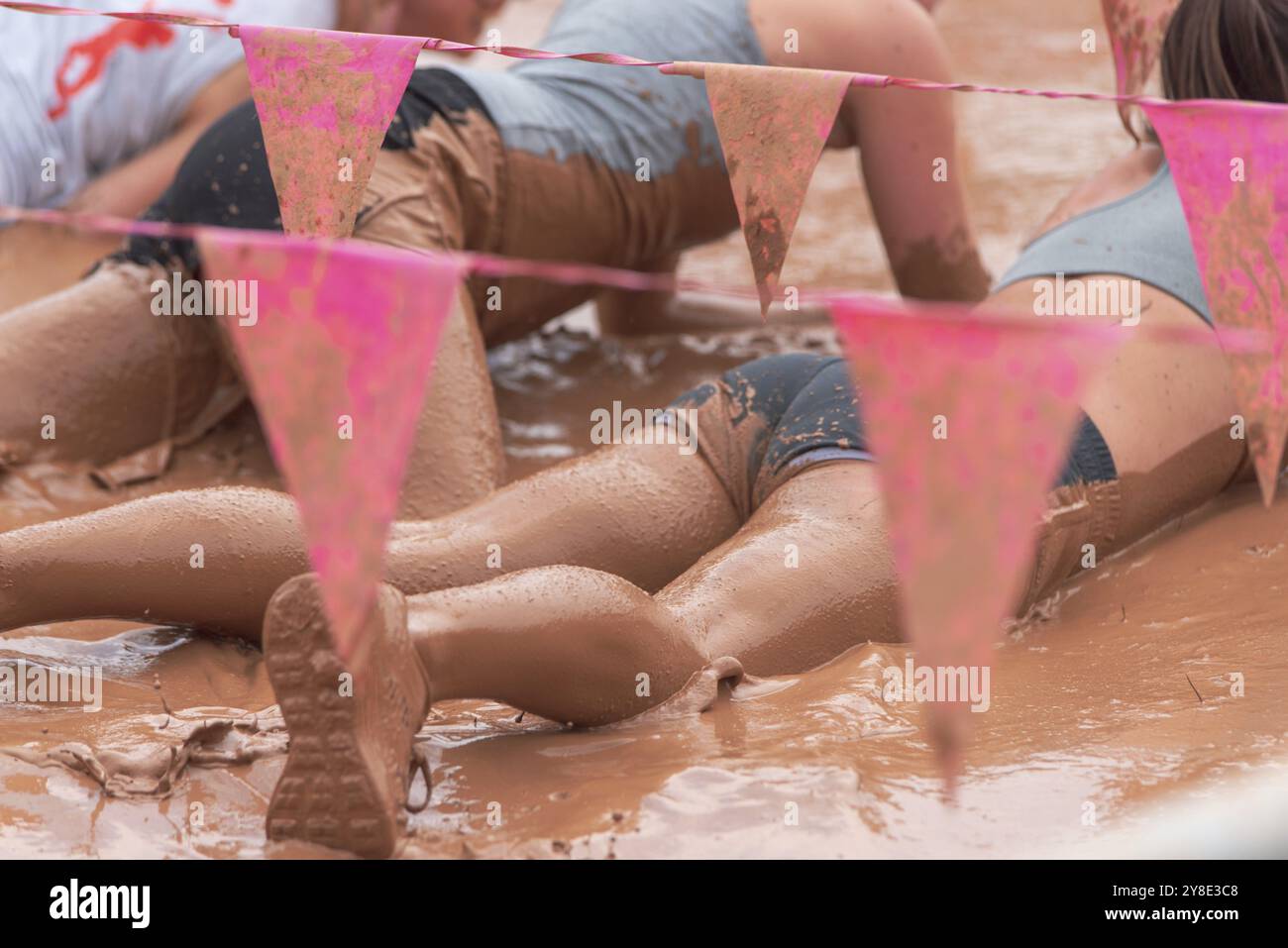 Leute, die bei einer Veranstaltung mit rosa Fahnen durch Schlamm kriechen Stockfoto